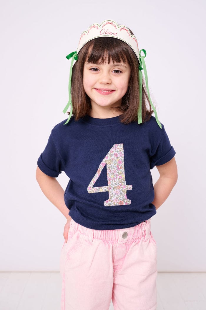 A smiling 4 year old girl wearing a birthday navy t-shirt with a liberty print number 4 on the front.
