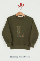 A khaki sweatshirt with an initial on the front. The initial is made from vintage cars Liberty print.