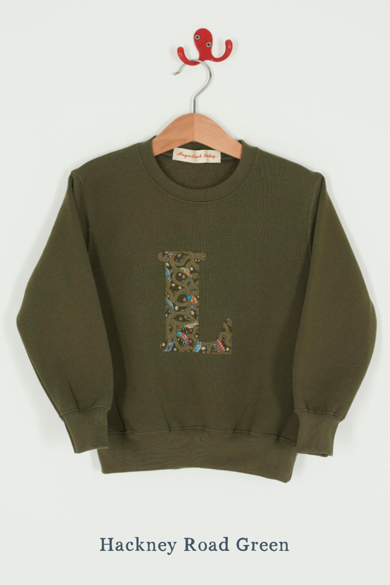 A khaki sweatshirt with an initial on the front. The initial is made from vintage cars Liberty print.