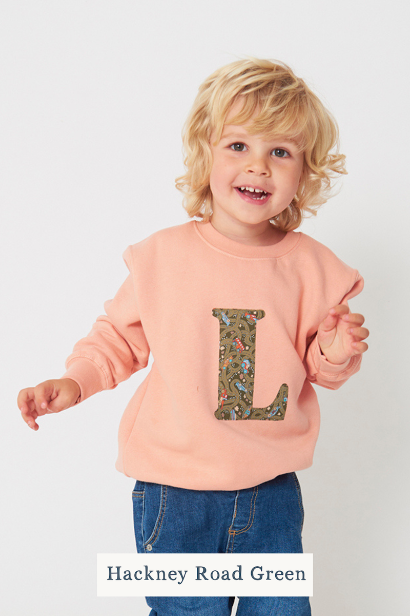 A pink personalised sweatshirt with an initial sewn on to the front. The initial is made from vintage car liberty print