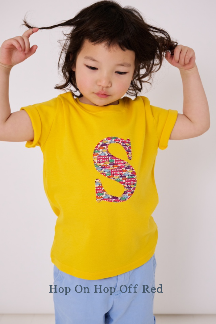 a smiling 3 year old boy wearing a yellow personalised t-shirt with his initial cut from cars liberty print on the front.