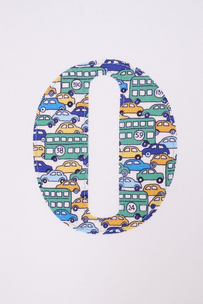 a close up of a personalised cotton baby romper with his initial on the front in hop on hop off liberty print featuring cars and London buses.
