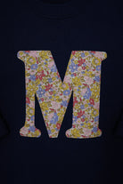 A close-up of a navy blue kids t-shirt featuring a large letter 'M' graphic filled with a Liberty print floral Juila Belle pattern.