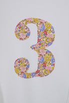 A large decorative number 3 filled with a dense multicolour floral Liberty print pattern, shown on a plain light background. A close up of a children's birthday t-shirt.