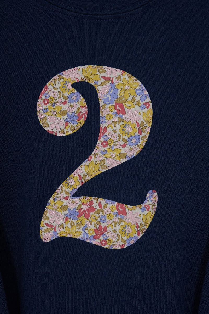 A close-up of a navy blue t-shirt featuring a large floral Liberty Julia Belle number '2' on the front. Showing a close up of he stitching.
