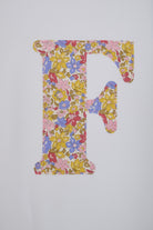 A decorative capital letter F filled with a dense floral  Liberty print in pink, yellow, blue, and red tones.