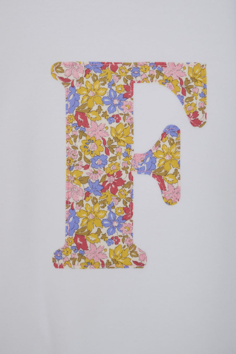 A decorative capital letter F filled with a dense floral  Liberty print in pink, yellow, blue, and red tones.