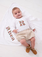 A newborn baby girl wearing a Personalised baby Bodysuit in Libby floral Liberty Print. She is laying on a personalised cotton baby blanket with her name sewn on.