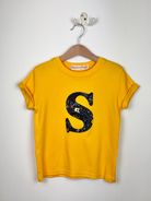 Yellow t-shirt with a large black letter 'S' on a hanger against a white background