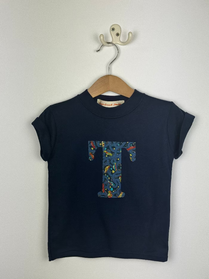 Navy blue t-shirt with a colourful  liberty car print letter 'T' on a wooden hanger against a white background