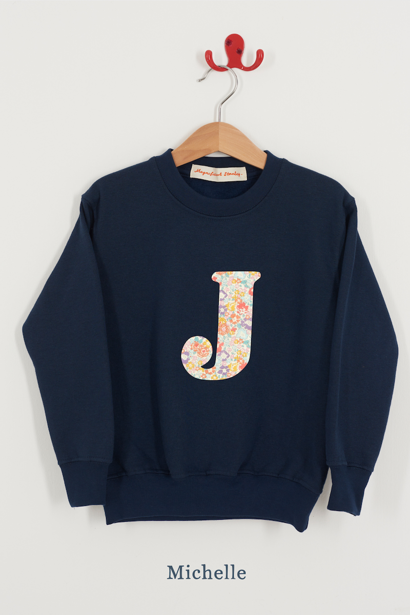Navy blue sweatshirt with floral letter 'J' on a hanger against a white background
