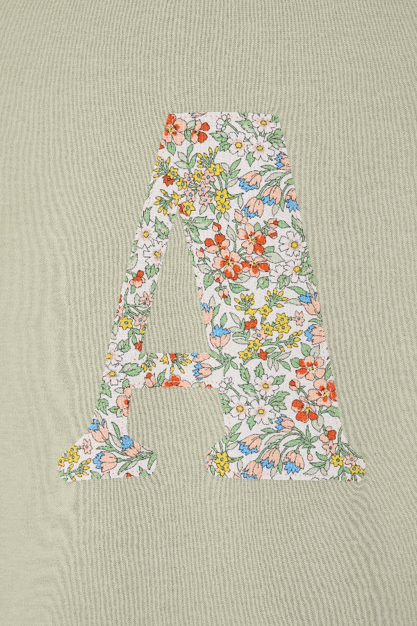 A personalised kids sage green t-shirt with his initial cut from Nazanin liberty print on the front.