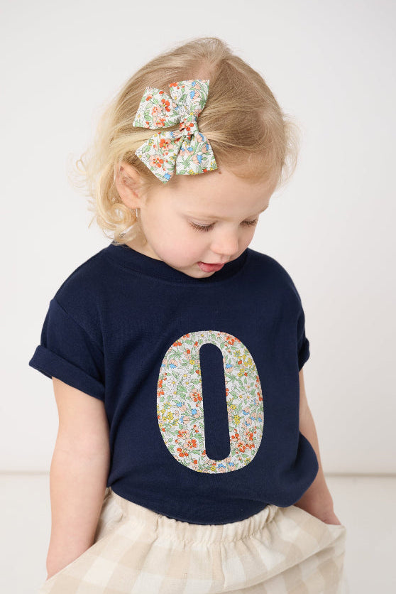 a 2 year old girl wearing a personalised kids navy t-shirt with an initial cut from nazanin liberty floral print on the front.