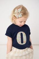 Child wearing a navy blue shirt with a floral number '0' on a white background