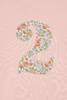 A Pink t-shirt with a Liberty Nazanin floral number '2', a close up of the stitching