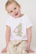 A 4 year old girl wearing a white cotton birthday t-shirt with the number 4 sewn on the front cut from liberty Nazanin fabric.