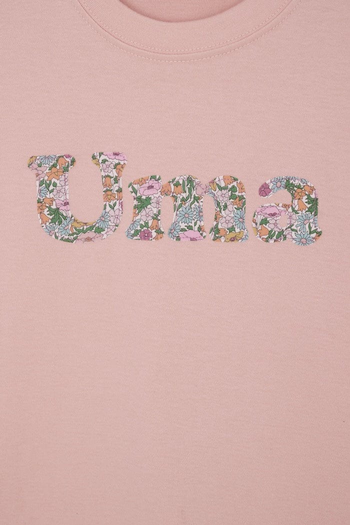A soft pink kids t-shirt with a name cut from Liberty print in lowercase letters.