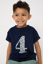 A 4 year old boy wearing a navy cotton t-shirt with the number 4 sewn on the front cut from liberty Quey 2 zoo animal print.