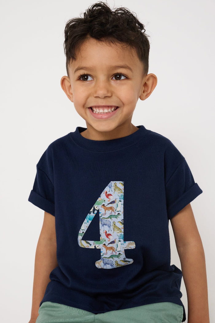 A 4 year old boy wearing a navy cotton t-shirt with the number 4 sewn on the front cut from liberty Quey 2 zoo animal print.