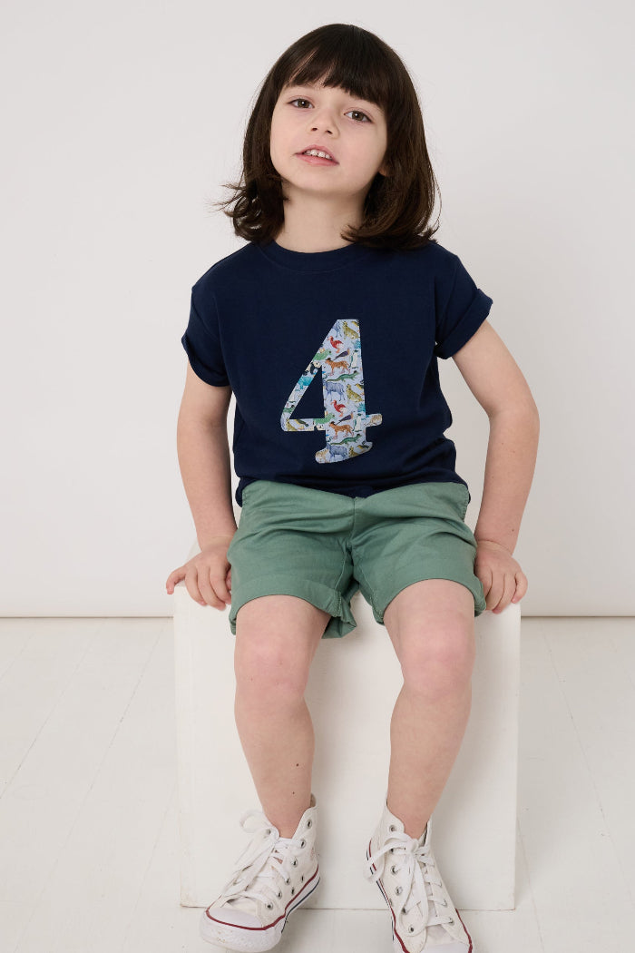 A 4 year old boy wearing a navy cotton t-shirt with the number 4 sewn on the front cut from liberty Quey 2 zoo animal print.