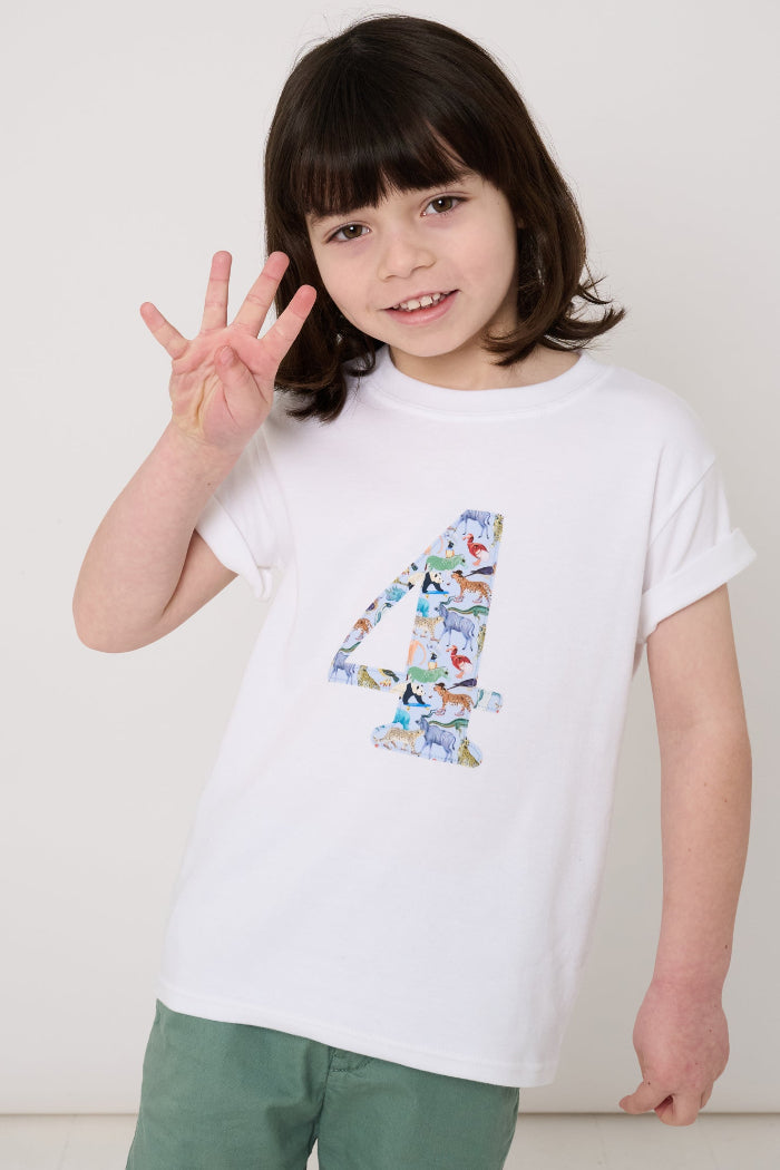 A 4 year old boy wearing a white cotton t-shirt with the number 4 sewn on the front cut from liberty Quey 2 zoo animal print.