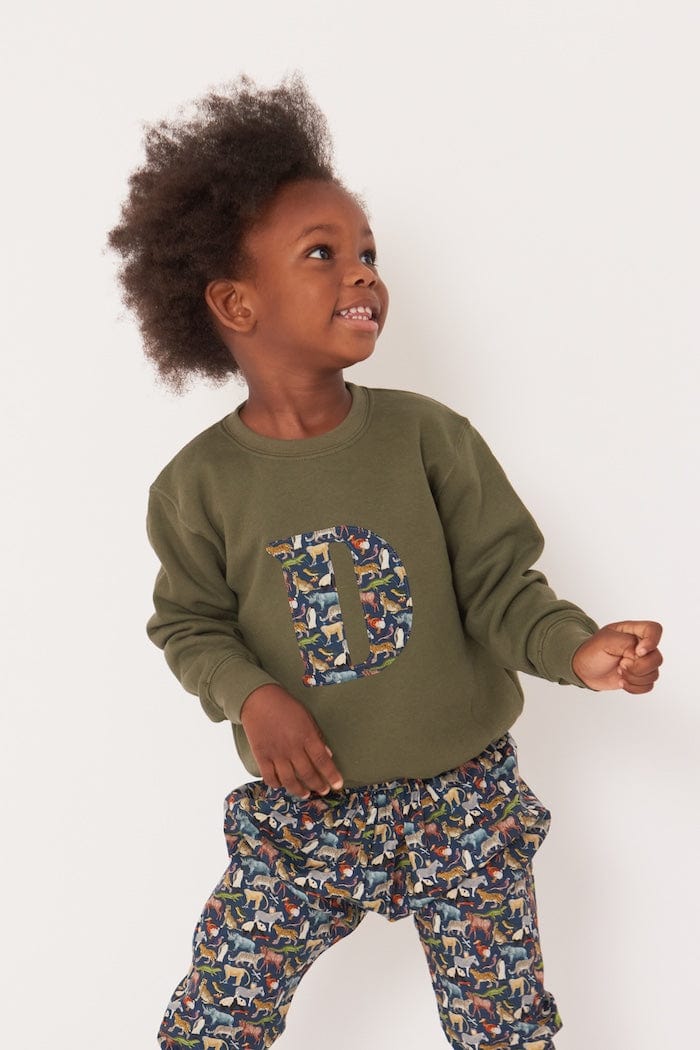 A 3 year old boy wearing a personalised  khaki sweatshirt with an initial made from quey 2 Liberty animal print fabric.