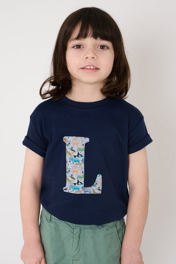 a 5 year old boy wearing a personalised kids navy t-shirt with an initial cut from Quey 2 liberty zoo animal print on the front.