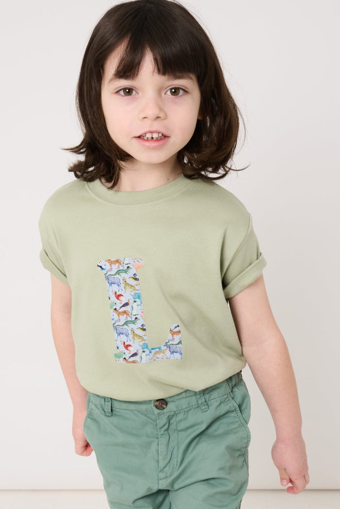 a 5 year old boy wearing a personalised kids sage green t-shirt with his initial cut from quey 2 zoo animal liberty print on the front.