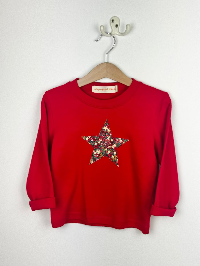 Red kids t-shirt with a floral star design on a hanger against a white background
