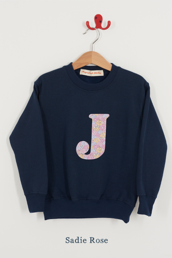 Navy blue sweatshirt with floral letter 'J' on a hanger against a white background