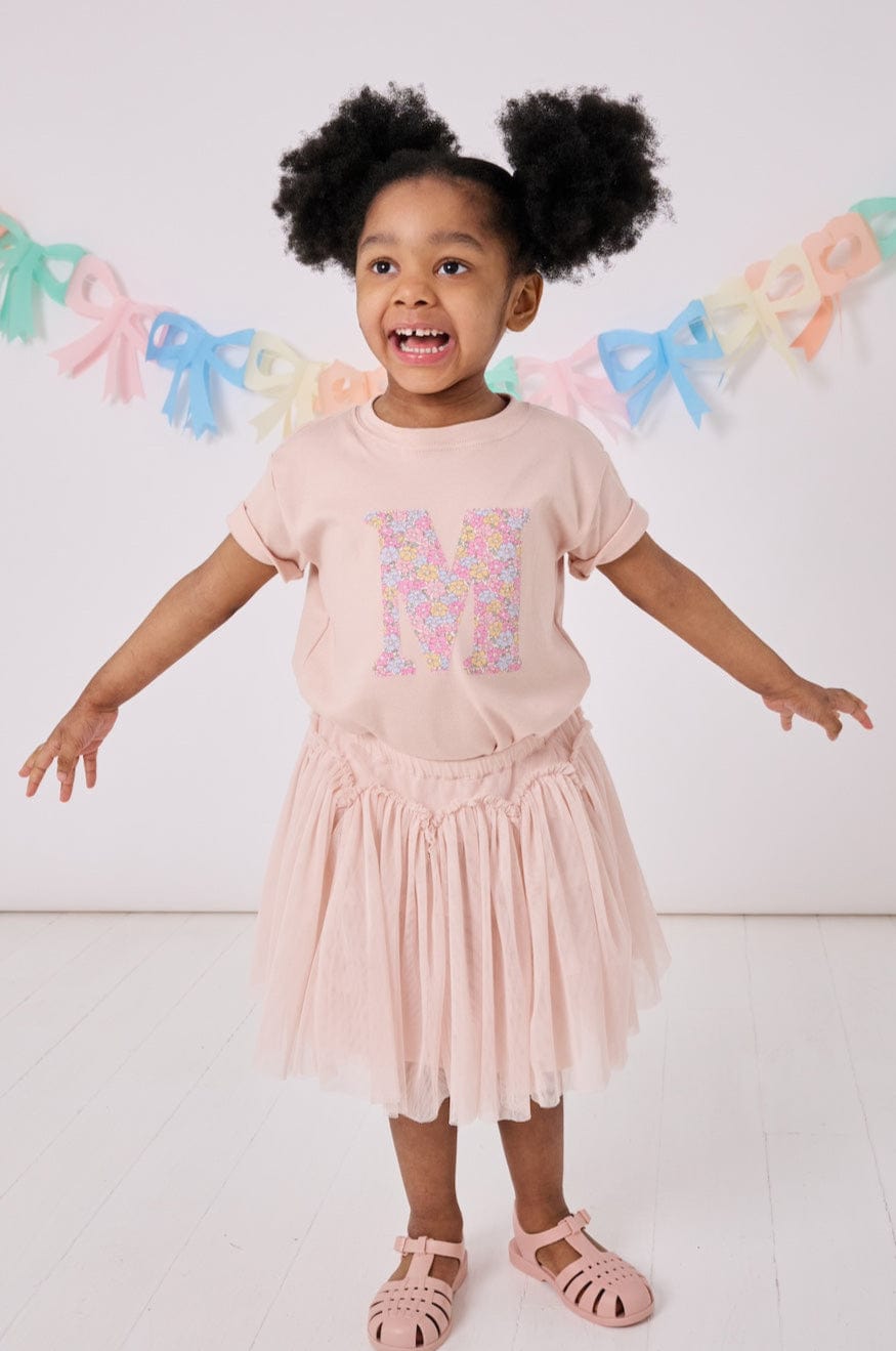 a little girl wearing a personalised kids pink t-shirt with an initial cut from sadie rose liberty floral print on the front
