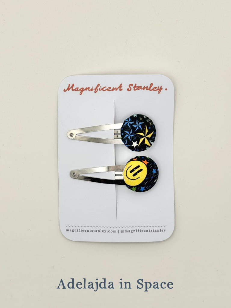 Two liberty bobble hair clips with colourful smiley face design in Adelajda in Space print on a 'Magnificent Stanley' card.