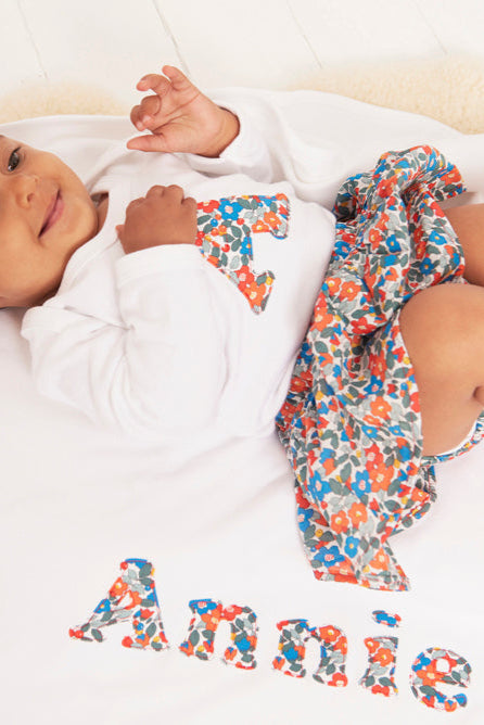 Baby lying on a white blanket with colorful liberty fabric and 'Annie' embroidered on it.