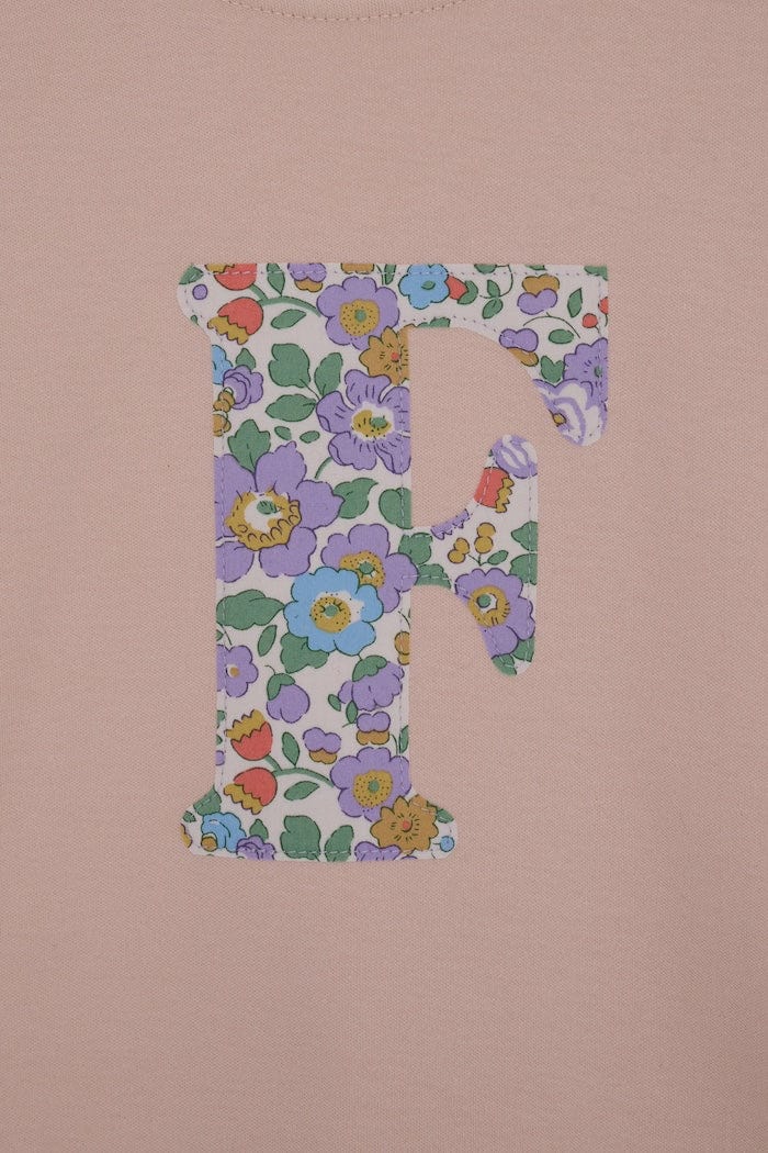 a close up of the appliqué stitching on a personalised kids blush pink  t-shirt with an initial cut from Betsy Purple liberty floral print on the front.
