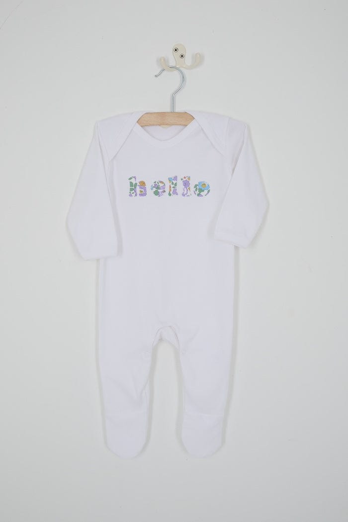 Close up of a white cotton romper with the word hello on it. the letters are cut from Betsy Purple liberty print and appliquéd onto the romper.