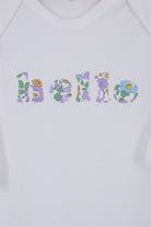 Close up of a white cotton romper with the word hello on it. the letters are cut from Betsy Purple liberty print and appliquéd onto the romper.