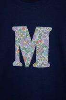 a personalised kids navy t-shirt with an initial cut from betsy purple liberty floral print on the front. Close up on the stitching. 