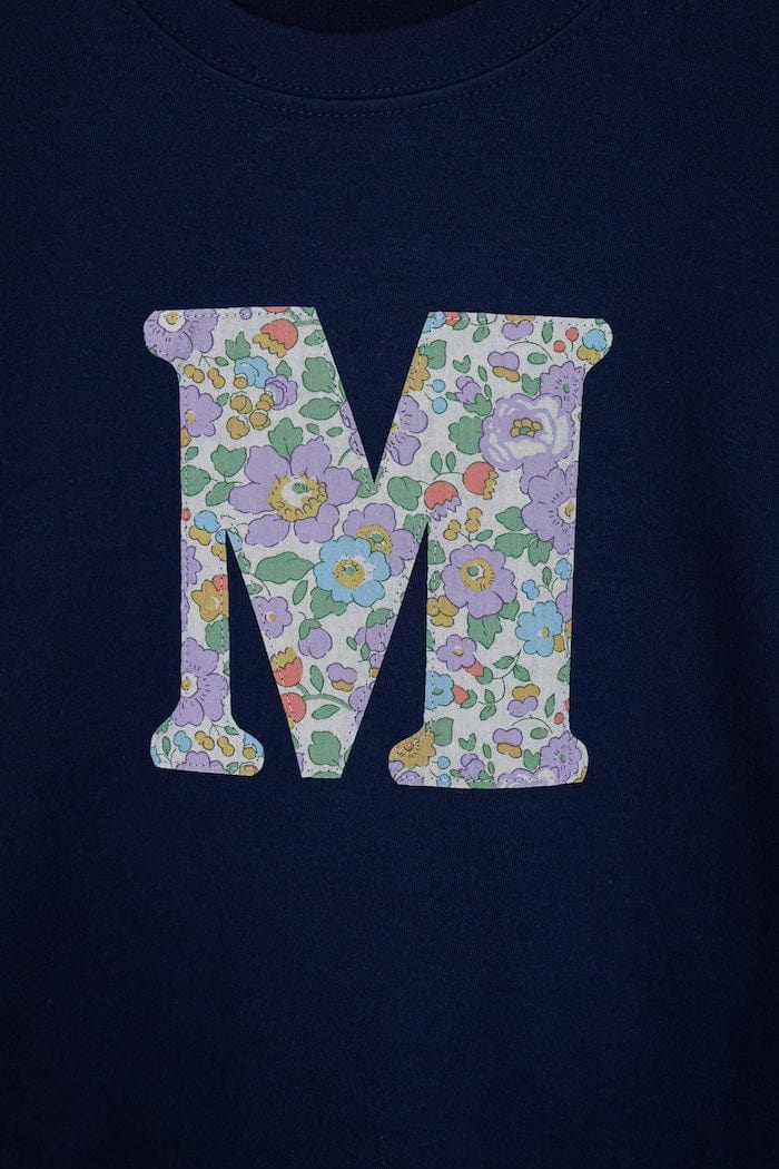 a personalised kids navy t-shirt with an initial cut from betsy purple liberty floral print on the front. Close up on the stitching. 