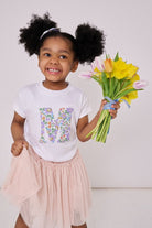 a 4 year old girl wearing a personalised kids white t-shirt with an initial cut from betsy purple liberty floral print on the front