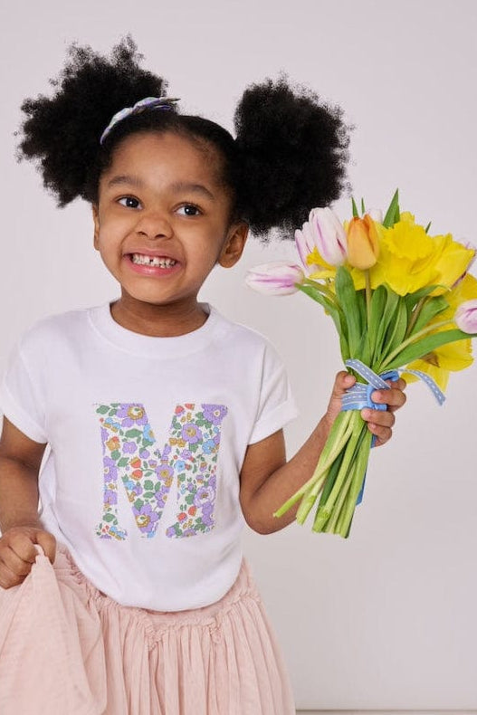 a 4 year old girl wearing a personalised kids white t-shirt with an initial cut from betsy purple liberty floral print on the front