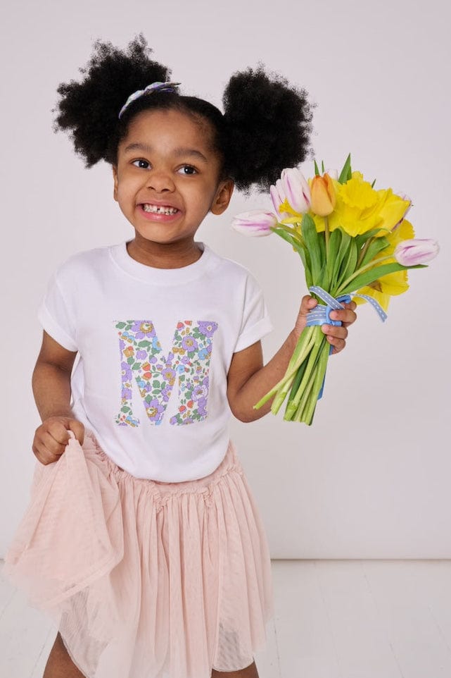 a 4 year old girl wearing a personalised kids white t-shirt with an initial cut from betsy purple liberty floral print on the front
