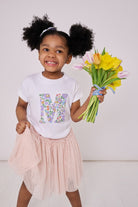 A 3 year old girl wearing a personalised white cotton t-shirt with her initial on in Betsy Purple floral Liberty fabric.