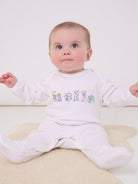 A 6 month old baby girl wearing a white cotton baby romper with the word hello made from Betsy Liberty Print sewn onto the front.