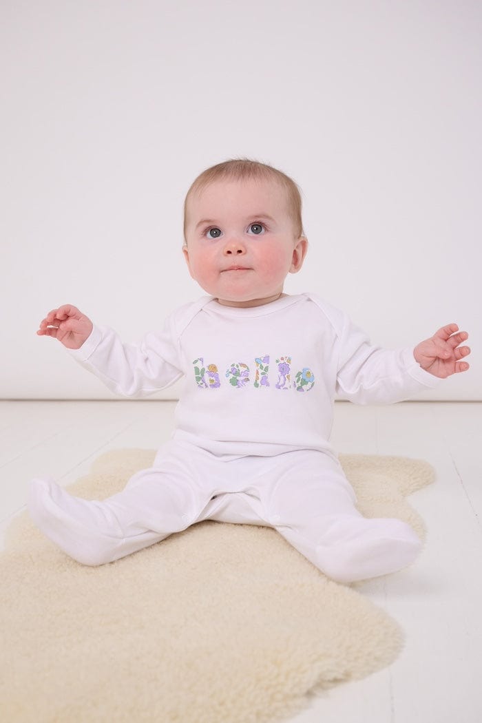 a baby wearing a white cotton romper with the word hello on it. the letters are cut from Betsy Purple liberty print and appliquéd onto the romper.