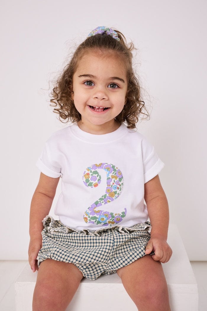 a 2 year old girl wearing a white birthday t-shirt with a number 2 cut from betsy purple liberty floral print on the front