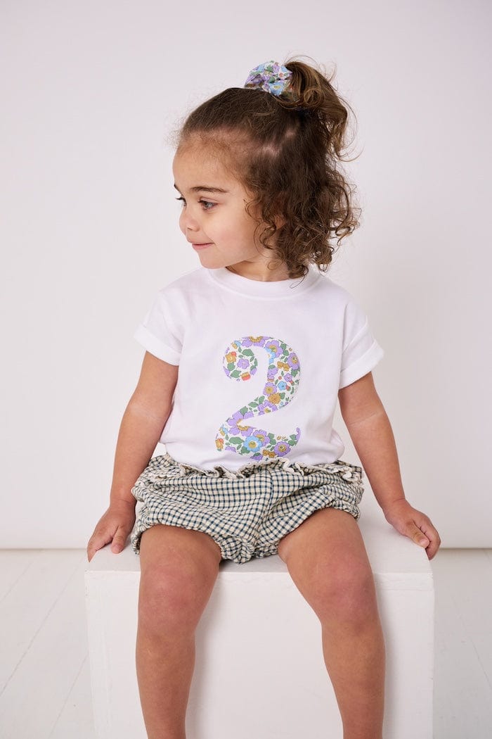 a 2 year old girl wearing a white birthday t-shirt with a number 2 cut from betsy purple liberty floral print on the front
