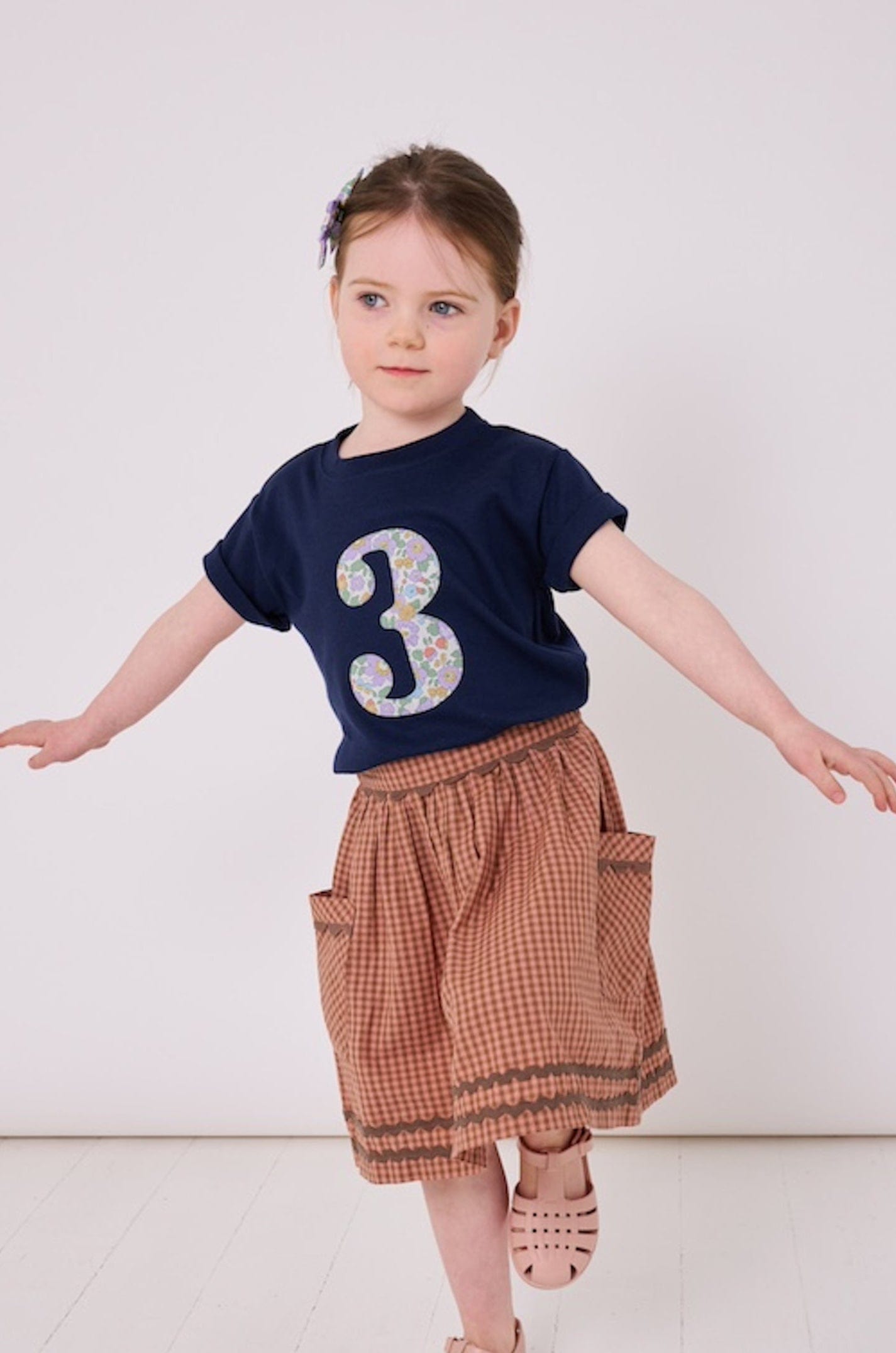 a 3 year old girl wearing a navy birthday t-shirt with a number 3 cut from liberty betsy purple floral print on the front