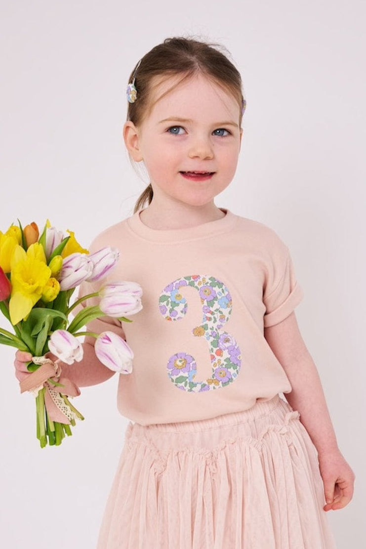 a 3 year old girl wearing a pink birthday t-shirt with a number 3 cut from betsy purple liberty floral print on the front