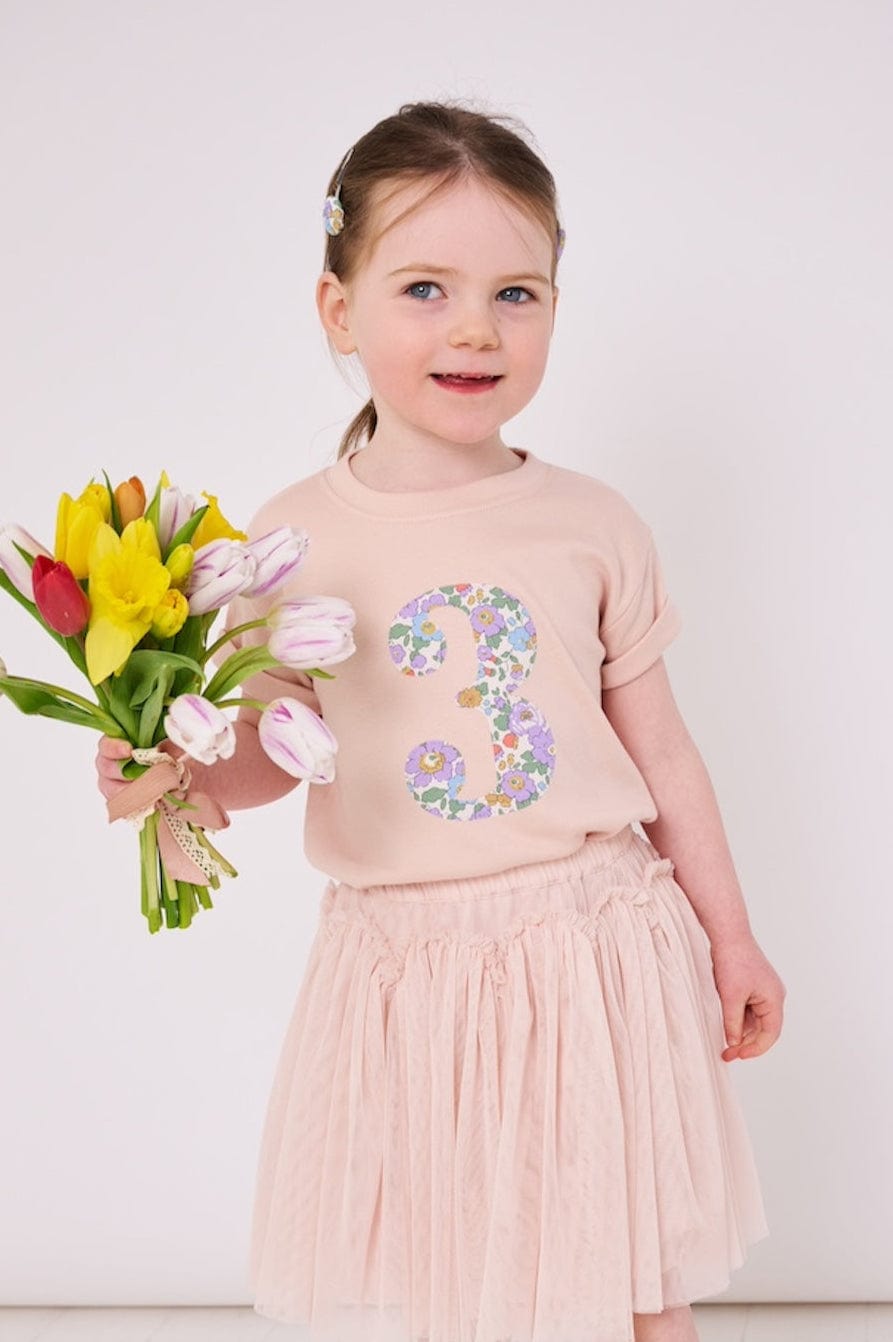 a 3 year old girl wearing a pink birthday t-shirt with a number 3 cut from betsy purple liberty floral print on the front