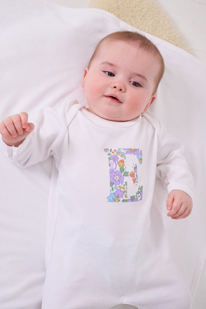 a happy baby wearing a cotton baby romper with her initial on the front in betsy purple floral liberty print. 